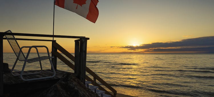 Photo of Canadian flag blowing in breeze over Lake Erie next to an outdoor lounge chair.