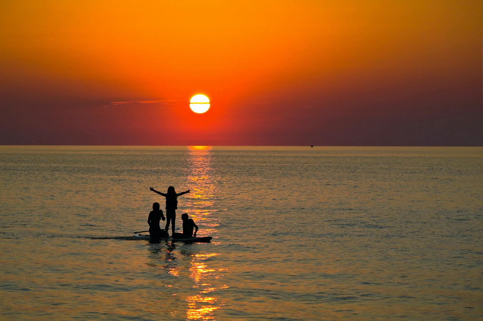 Three people on a paddle board in Lake Erie at sunset