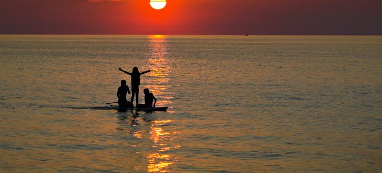 Three people on a paddle board in Lake Erie at sunset