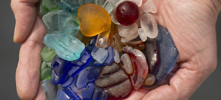 A close-up shot of two hands holding about two dozen small pieces of beach glass.